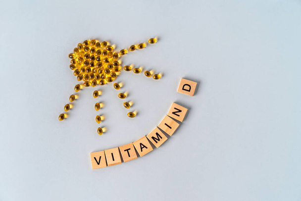 Надпись "Витамин D" из деревянных блоков и желтых таблеток в виде солнца, концепция получения витамина через солнце - Фото, изображение