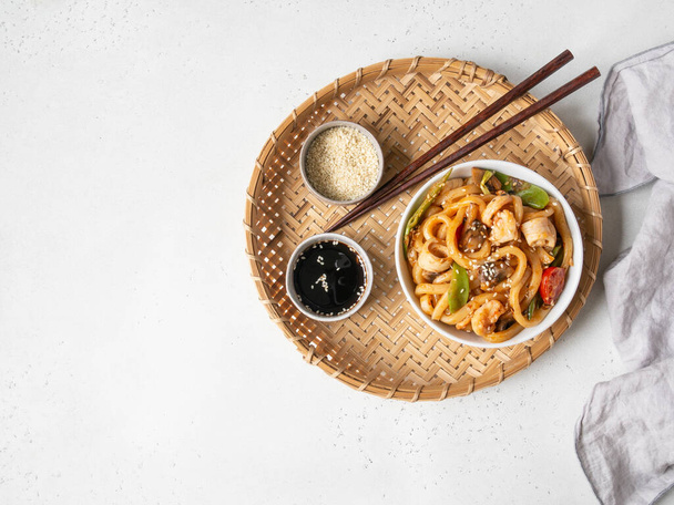 Macarrão Udon com frutos do mar e legumes cozidos em um wok em uma tigela branca em uma bandeja de vime. Vista superior. Espaço de cópia - Foto, Imagem