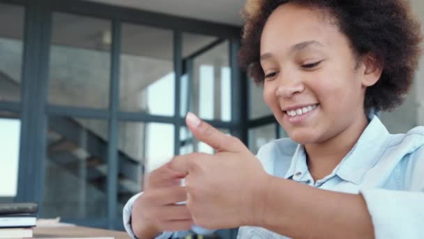 Learning activities. Happy african american teenage girl counting on fingers and smiling while communicating with teacher through video chat app during online lesson at home - Footage, Video