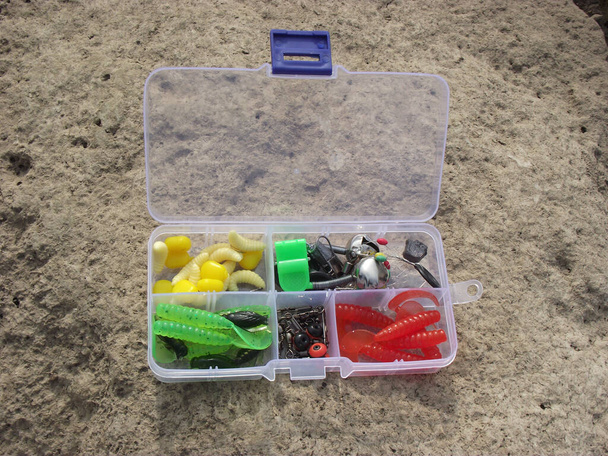 on the rocky shore, on one of the large stones, there are fishing tackle in a plastic box divided into sections - Photo, Image