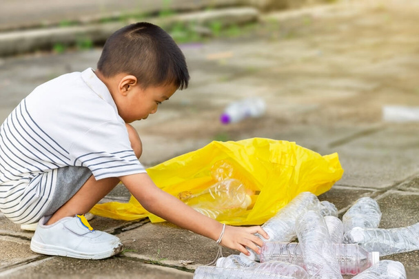 市の公園で。アジア系の少年は、現場を掃除するボランティアです。彼は地面にたくさんのペットボトルやわらを拾いました。環境の保全と廃棄物の削減. - 写真・画像