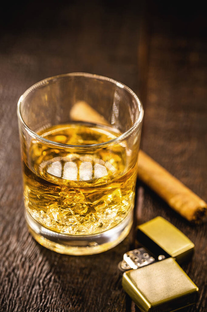 whiskey of bourbon, gedistilleerde drank met mout in een glas met ijsblokjes, met aan de zijkant een sigaar. Tijd om te ontspannen, levensstijl - Foto, afbeelding