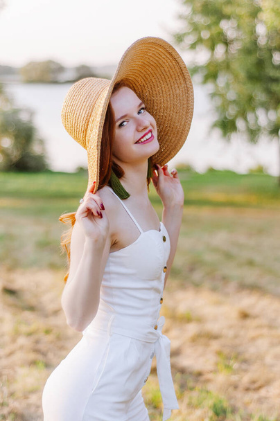 Close up portrait of a beautiful red hair girl in a pink vintage dress and straw hat standing near colorful flowers. Art work of romantic woman .Pretty tenderness model looking at camera. - Foto, Imagem