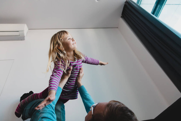 щаслива мила маленька дівчинка літає в руках батьків у спальні, одинокий тато піднімає милу маленьку доньку
 - Фото, зображення