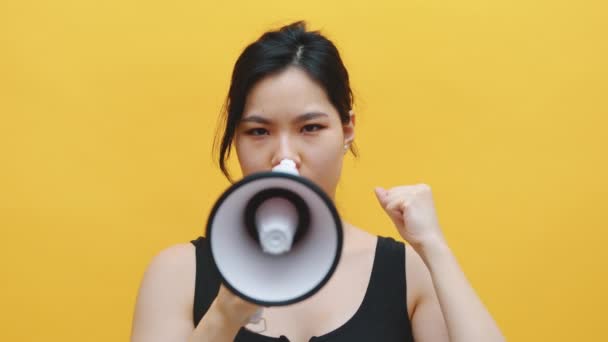 Eine junge Studentin spricht im Studio mit einem Megafon in die Kamera. Vereinzelt auf gelbem Hintergrund - Filmmaterial, Video