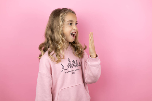 Young beautiful child girl standing over isolated pink background surprised with her hands over her mouth - Foto, afbeelding