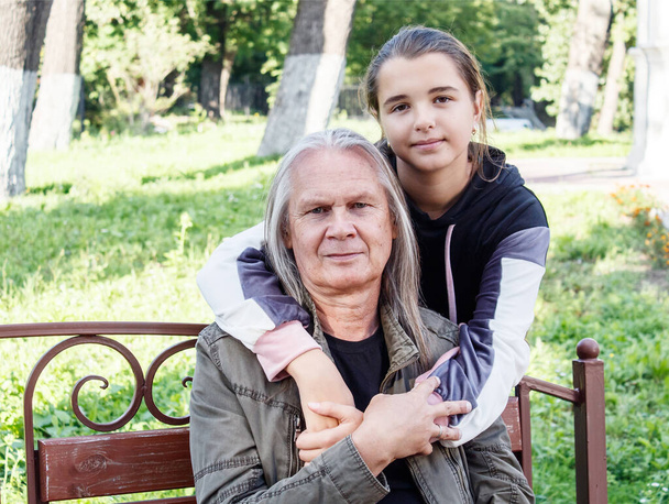 Enkelin umarmt ihren Großvater an einem sonnigen Herbsttag auf einer Bank im Stadtpark - Foto, Bild