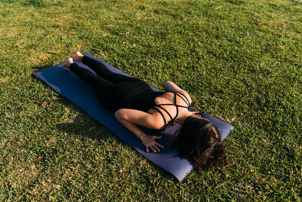 Mujer acostada en su esterilla haciendo yoga en la hierba al aire libre - Foto, Imagen