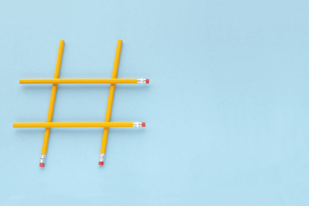 Hashtag sign made from yellow pencils on a blue background with copy space, top view. Wooden yellow pencils on a blue background with copy space. Hashtag is popular on the internet. Minimalism - 写真・画像