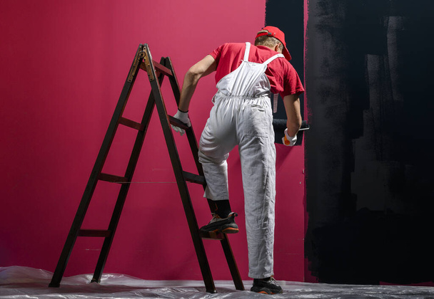 Egy ember, aki falat fest. Festő piros általános festés fal fekete színű - Fotó, kép