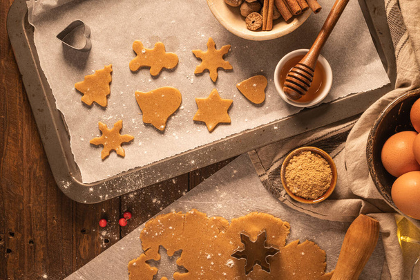 Making christmas gingerbread cookies. Raw dough in shape of gingerbread man, christmas tree, star, snowflakes on paper on tray on rustic table with rolling pin. Preparing for baking - Фото, зображення