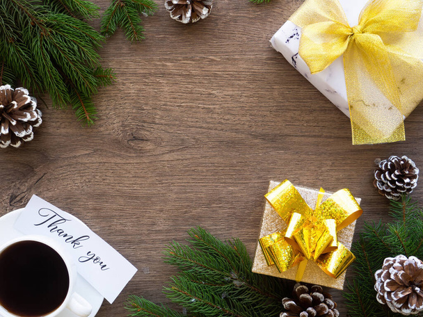 Ramas de árbol de Navidad con conos de abetos y caja de regalo con taza de café, nota con un mensaje. Fondo de madera. Concepto de vacaciones. Vista superior - Foto, Imagen