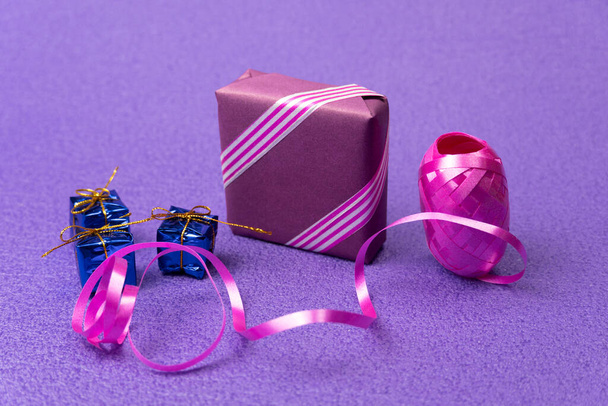 Cadeau dans une boîte violette et un ruban décoratif à côté d'un fond violet - Photo, image
