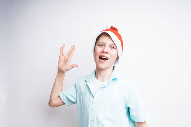 Cheerful caucasian boy wearing a Santa Claus hat is showing a Vulcan "spock" salute - Photo, Image