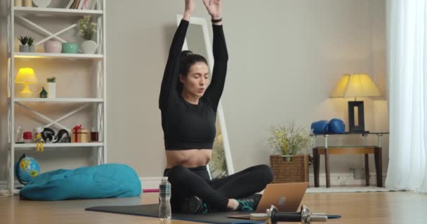 Wide shot portrait of beautiful young yogi sitting in lotus pose and doing breathing exercises using video lesson on laptop. Slim gorgeous Caucasian woman training at home. Cinema 4k ProRes HQ. - Filmati, video