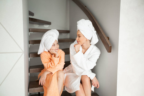 beautiful mom with daughter in bathrobes sitting on the stairs at home - Fotó, kép