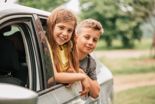 Two happy kids are waving their hands through their car windows.The brother and the sister are having fun travelling. - 写真・画像
