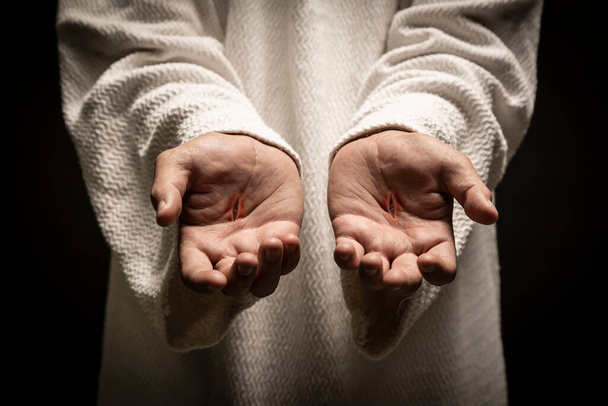 Jesus of Nazareth showing the wounds on his hands while praying on a dark night after being resurrected. - Foto, afbeelding