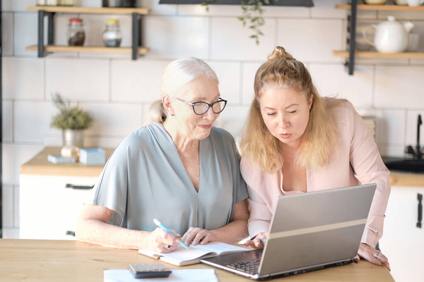 daughter helps her elderly mother figure it out online with her personal account. Woman teaching senior mother to use internet at home. Senior woman with her daughter looking at modern gadget indoors. - Fotoğraf, Görsel