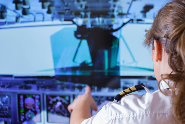 Красивая женщина-пилот в униформе с эполетами меняет настройки автопилота в кабине летающего самолета - Фото, изображение