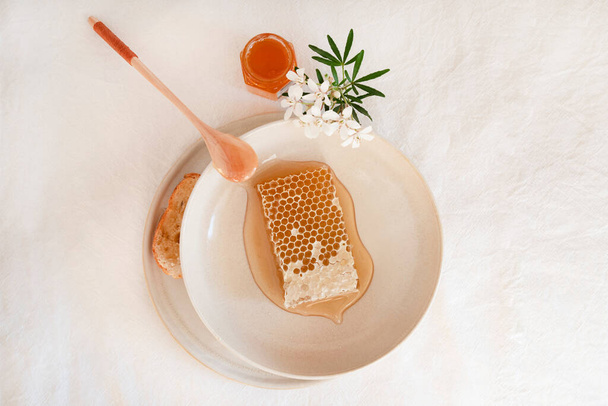 Honey and honeycomb on a white table with white flowers - Foto, Bild
