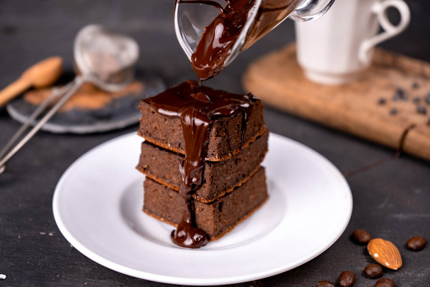 Brownies al cacao versati con cioccolato fondente fuso su un piatto bianco. Fondo nero - Foto, immagini