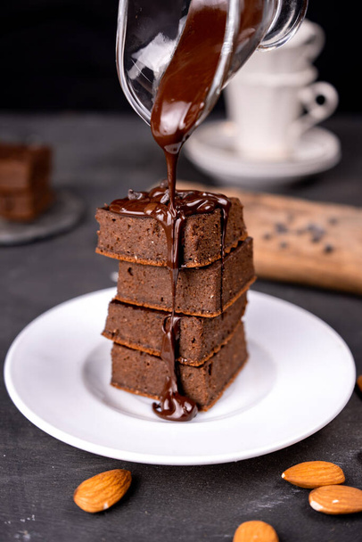 Kakao-Brownies mit geschmolzener dunkler Schokolade auf einem weißen Teller. Schwarzer Hintergrund - Foto, Bild