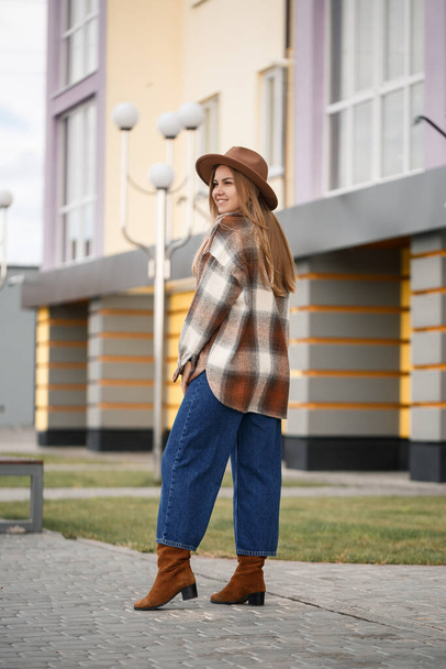 Beautiful girl with long hair in a brown hat and a plaid shirt. Young stylish woman in coat - Photo, Image