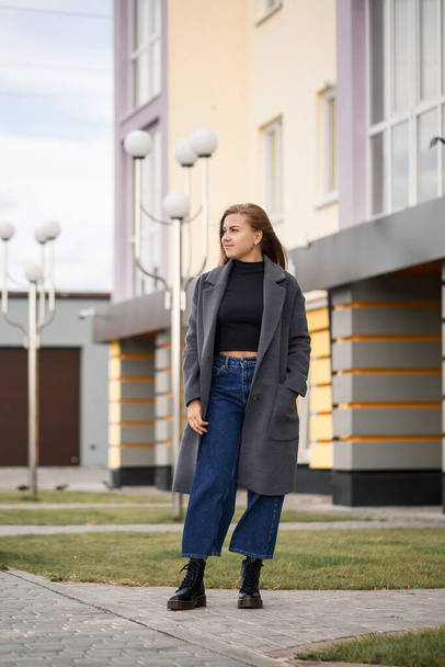 A beautiful girl with long hair in a black warm sweater and a gray coat on the street. Young stylish woman in autumn shoes - Fotografie, Obrázek