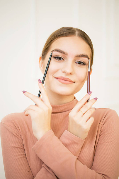 Girl apply a brush with a cosmetic product to her eyebrows. Beautiful cute girl smiles and makes eyebrow makeup - Foto, Bild