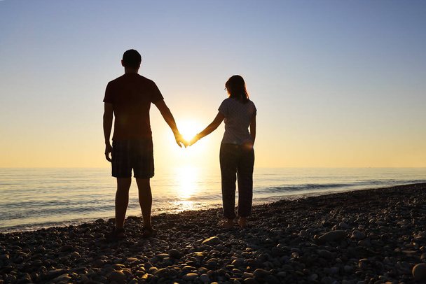 Coppia amorevole si tiene per mano nei raggi del sole al tramonto sulla riva del mare. Concetto di amore e felicità insieme - Foto, immagini