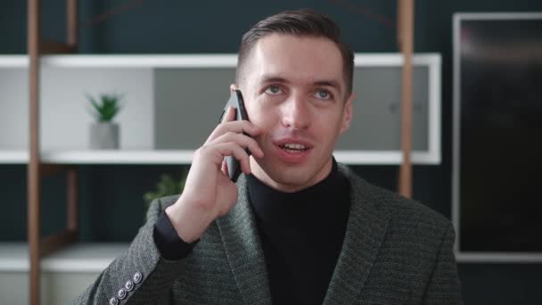 Portret van een zelfverzekerde zakenman aan het praten op een mobiele telefoon in een modern kantoor. Close-up vrolijke mannelijke ondernemer met een telefoontje op de werkplek. - Video