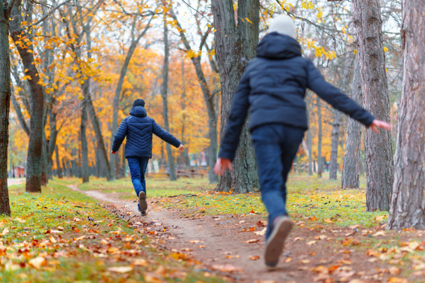 teen girl and boy running through the park and enjoys autumn, beautiful nature with yellow leaves - Photo, Image