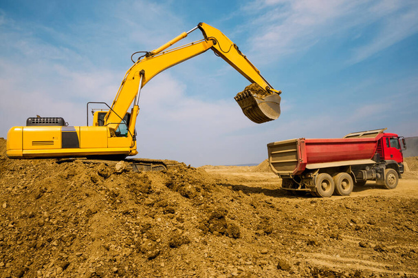 Earthworks, the excavator loads soil into the body of a cargo dump truck - Foto, Imagen