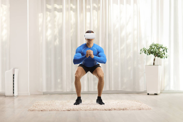 Muscular guy exercising with a virtual reality headset at home - Фото, изображение