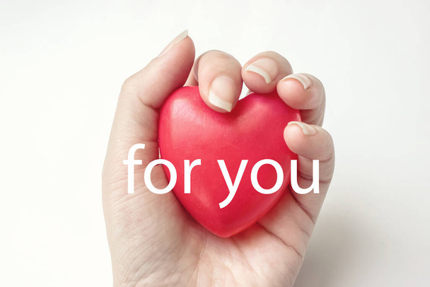 Woman hand hold red heart on the white background with text FOR YOU. Health insurance, donation, saving life concept - Photo, Image