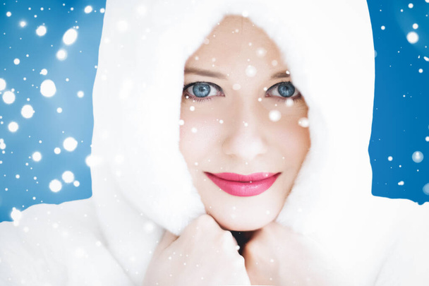 Happy Christmas and winter holiday portrait of young woman in white hooded fur coat, snow on blue background, fashion and lifestyle - Photo, Image