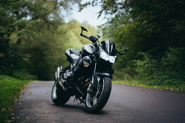 Casal jovem, cara e menina perto de uma motocicleta esportiva preta, em roupas de couro preto, na estrada na floresta - Foto, Imagem