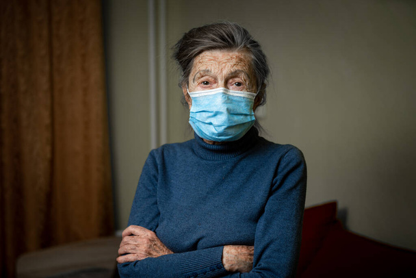 Der kluge Blick einer alten Frau mit medizinischer Maske auf dem Gesicht ermutigt Sie, Abstand zu halten und Schutzausrüstung zu tragen, Gesundheitsschutz während einer covid 19. Porträt einer Seniorin, die in die Kamera blickt, Altenpflege - Foto, Bild