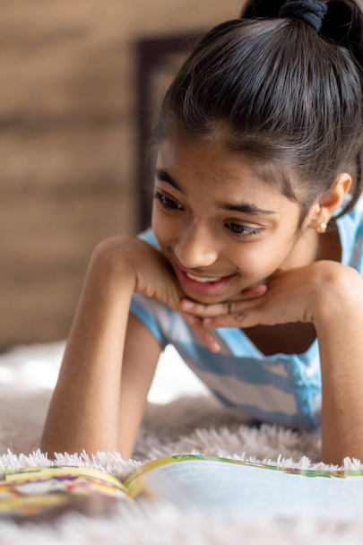 childhood, emotions, solitude, beauty concept - portrait of happy young minor cheerful joyful dark-skinned girl of middle eastern persian appearance 6-9 years old smiling cutely lying on bed indoors. - Photo, Image