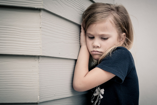 Portrait of sad little girl sitting near  wall in the day time - Foto, afbeelding