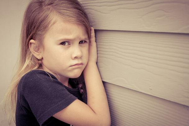 Portrait of sad little girl sitting near  wall in the day time - Foto, afbeelding