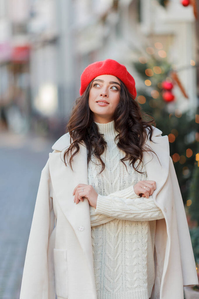 Portrait of a young beautiful woman in a red beret in a European city. Young woman holds a paper bag with baguettes. Christmas. - Photo, image