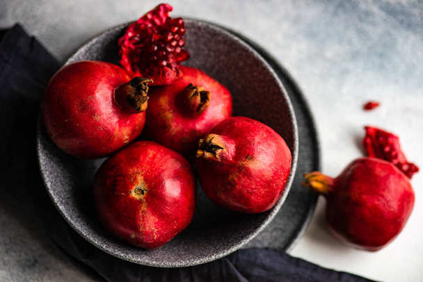 Organické granátové jablko ovoce s jeho semeny na talíři na šedém pozadí jako koncepce organických potravin - Fotografie, Obrázek