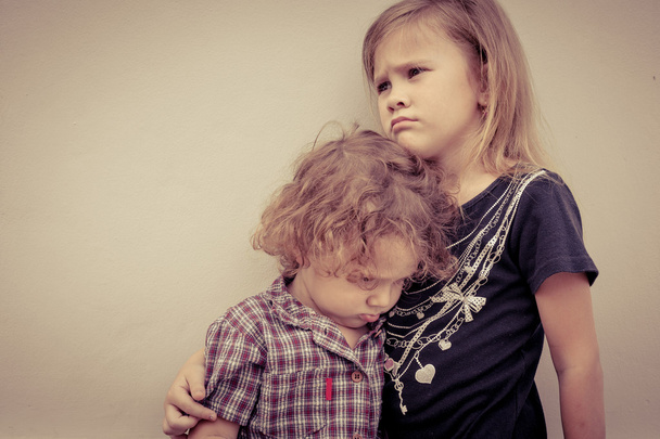 Porträt eines traurigen kleinen Mädchens und eines kleinen Jungen, die in der Nähe einer Mauer stehen. - Foto, Bild