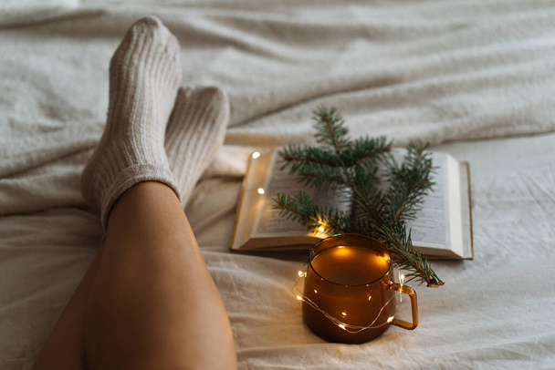 Femme est couché pieds sur la couverture blanche et shaggy livre de lecture. Confortable scène de loisirs. Femme relaxante à la maison - Photo, image