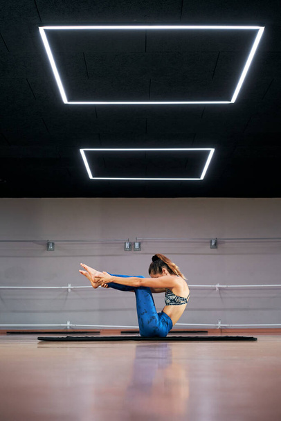 Jolie jeune femme pratiquant le yoga ou le pilates dans une salle de gym, faisant de l'exercice en vêtements de sport bleus, faisant la pose navasana - Photo, image