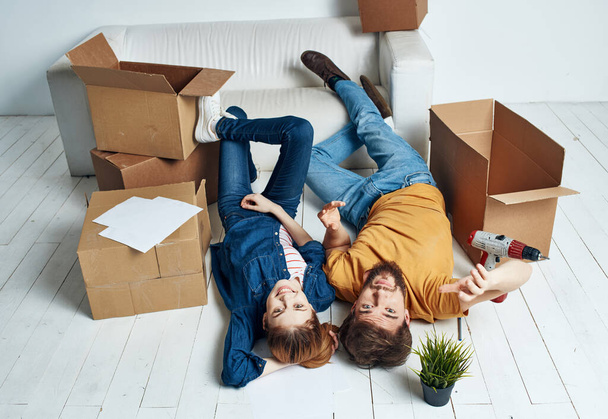 a man and a woman lie on the floor among boxes and a flower in a pot moving - 写真・画像