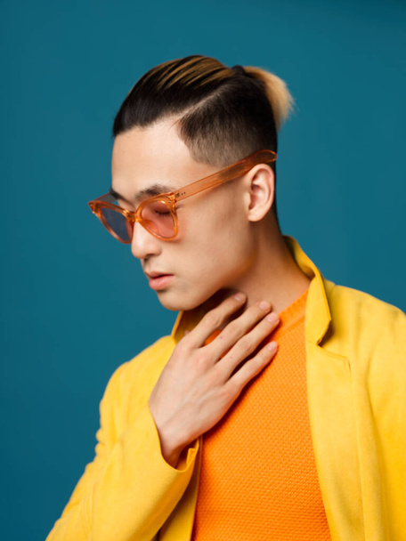 A man touches his neck with his hand on a blue background. Asian appearance hairstyle glasses - Foto, imagen
