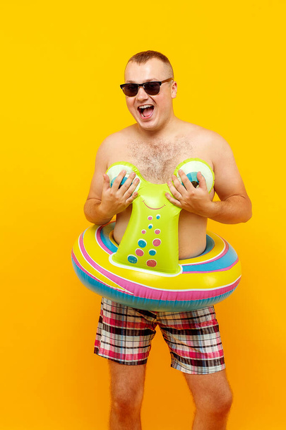 Adult topless man in rubber ring form of snail and sunglasses posing on yellow background. Isolate - Photo, image
